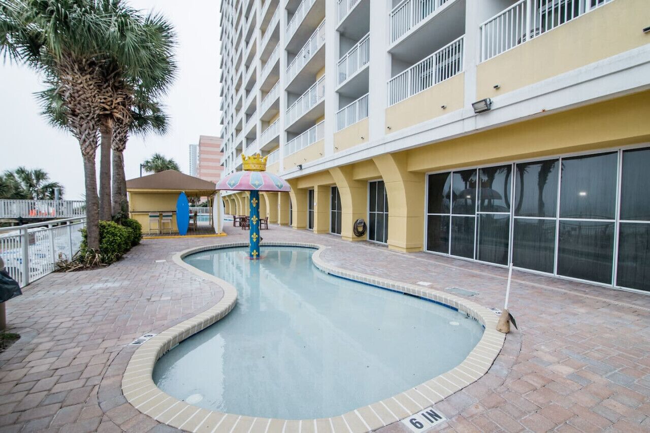 A swimming pool with a palm tree and a building with balconies.