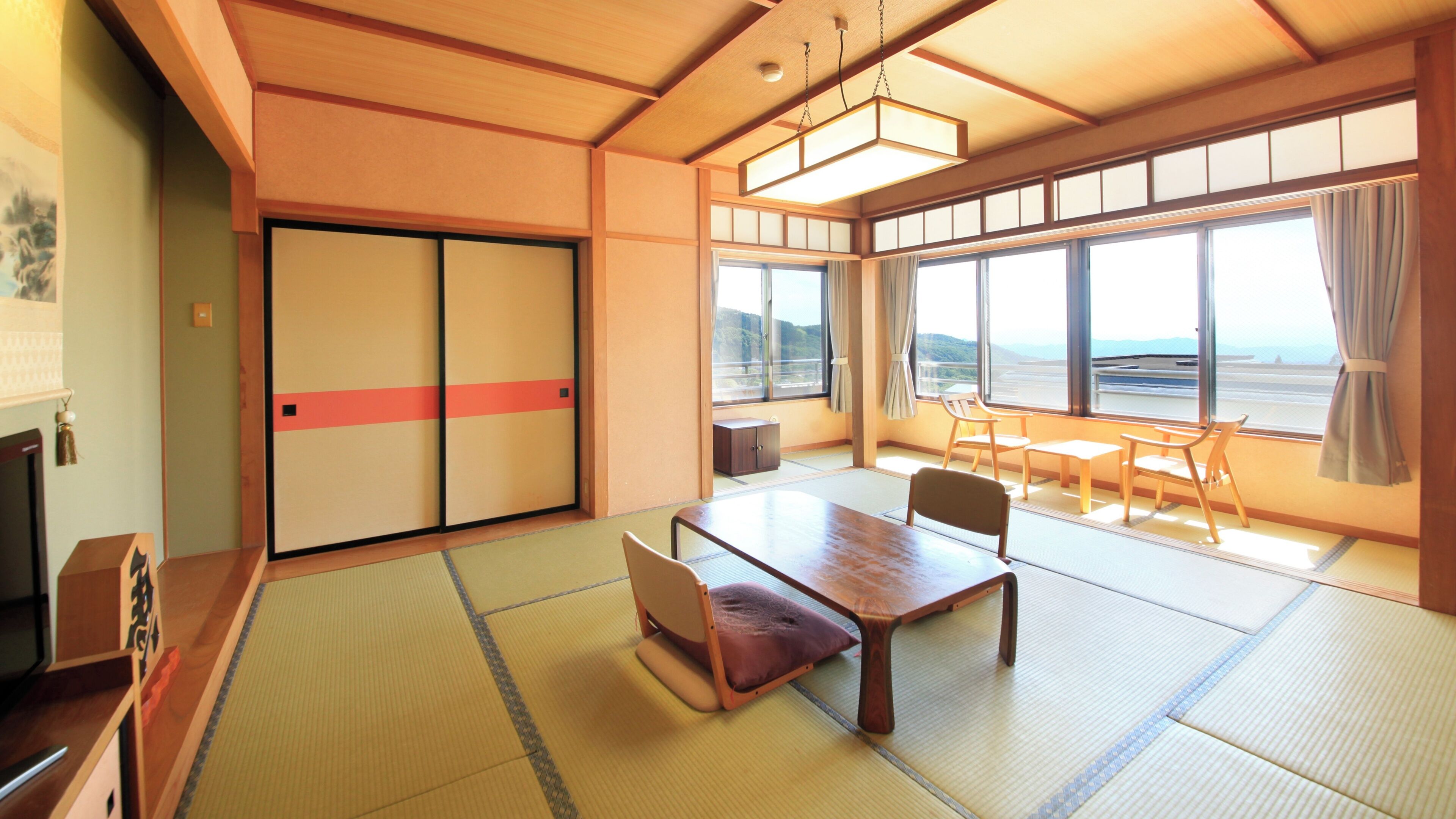 A traditional Japanese room with tatami flooring, a low table, chairs, a sliding door, and large windows with a view.