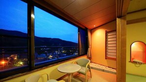 Un balcon avec une table et des chaises, une vue sur le paysage urbain au crépuscule et une fenêtre avec des stores.