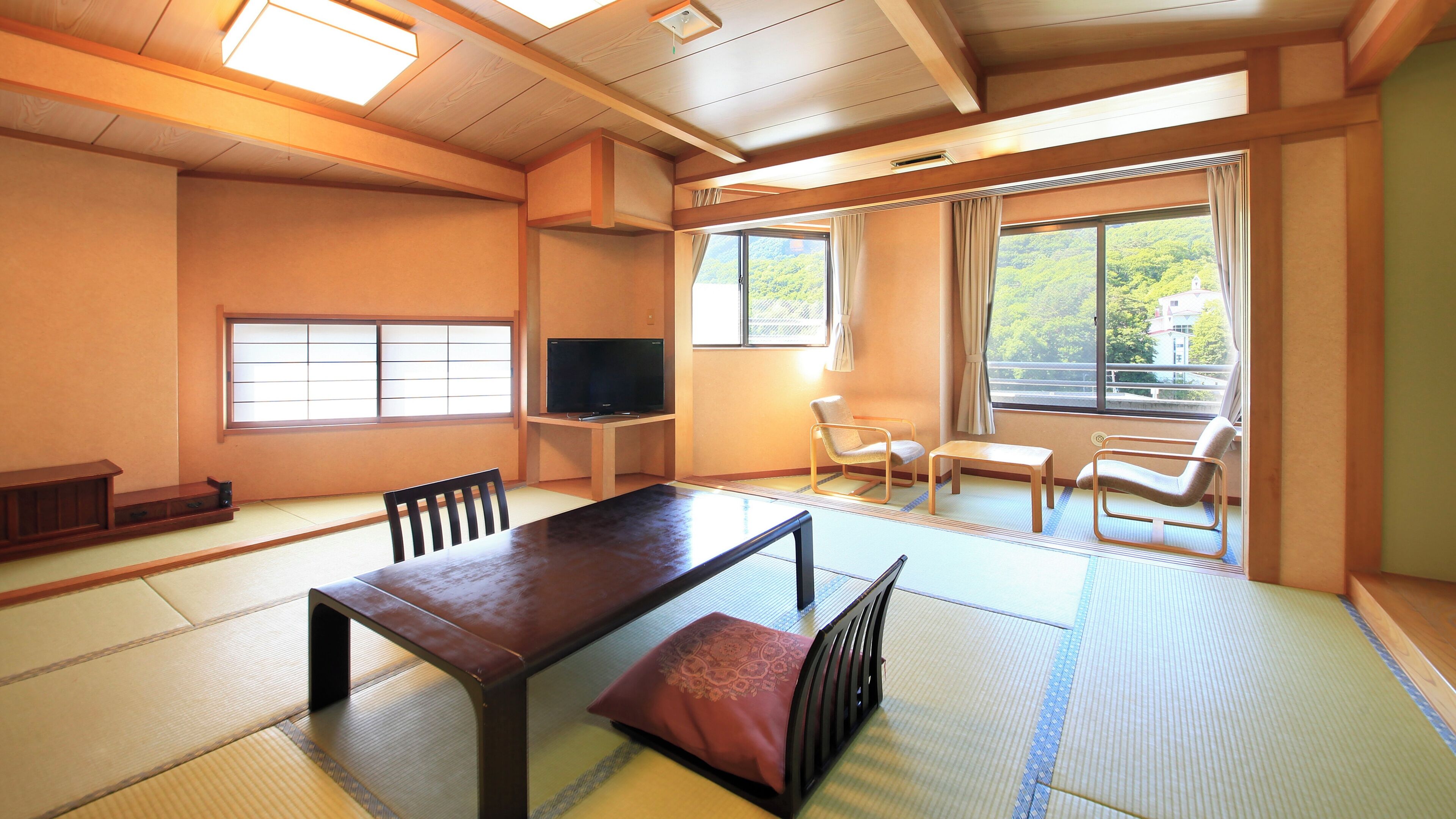 A traditional Japanese-style room with tatami flooring, a low table, chairs, a television, and large windows with curtains.