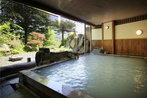 A traditional Japanese onsen with a view of a forested area and a stone bath. - Zao Plaza Hotel (Yamagata)