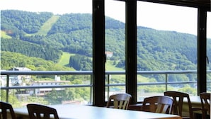 Un coin repas avec une table et des chaises, de grandes fenêtres donnant sur une colline boisée.