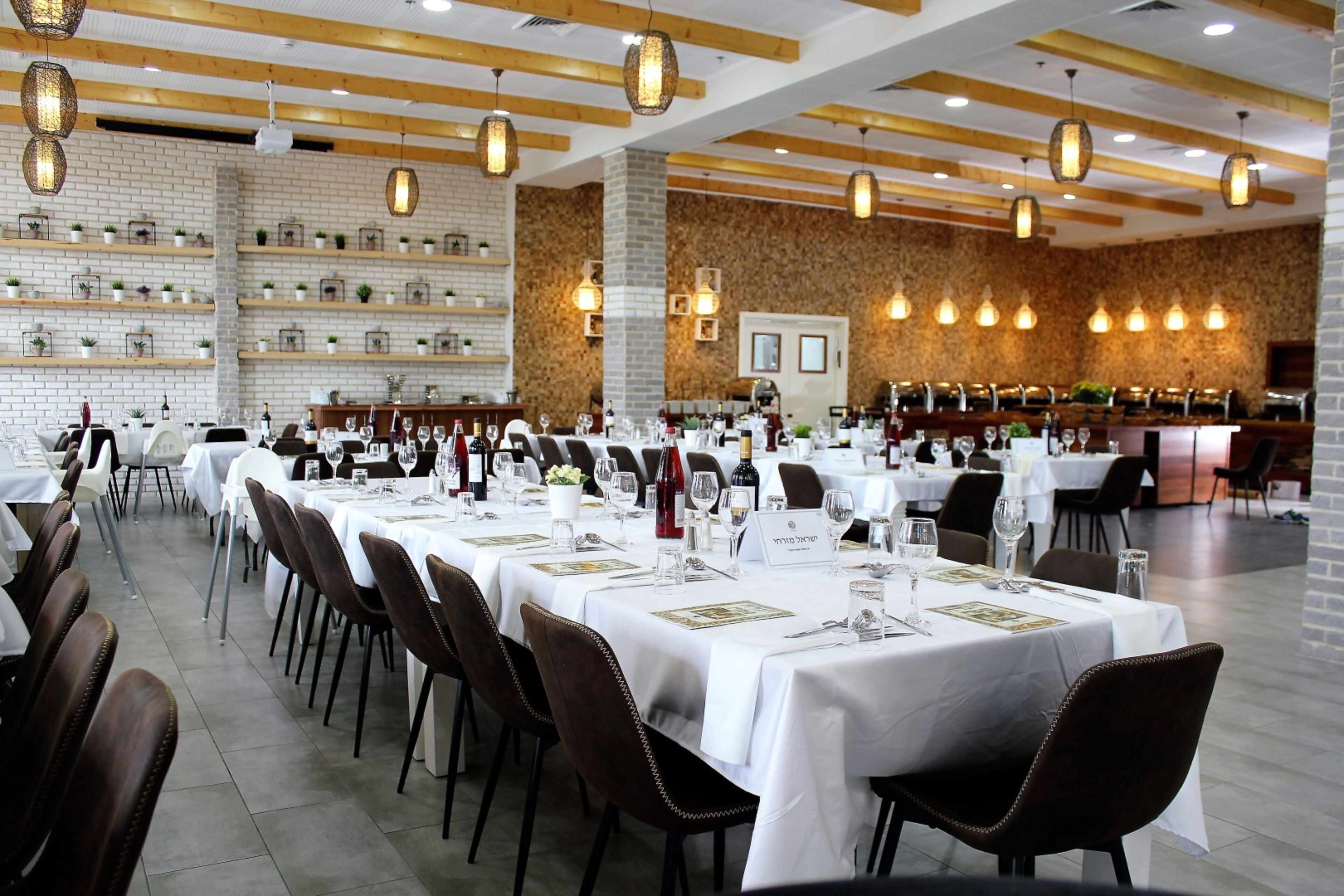 A restaurant with multiple dining tables set for guests, featuring white tablecloths and brown chairs.