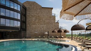 Un espace piscine moderne avec une piscine à l’eau d’un bleu limpide, des chaises longues et un bâtiment en pierre doté de grandes fenêtres.