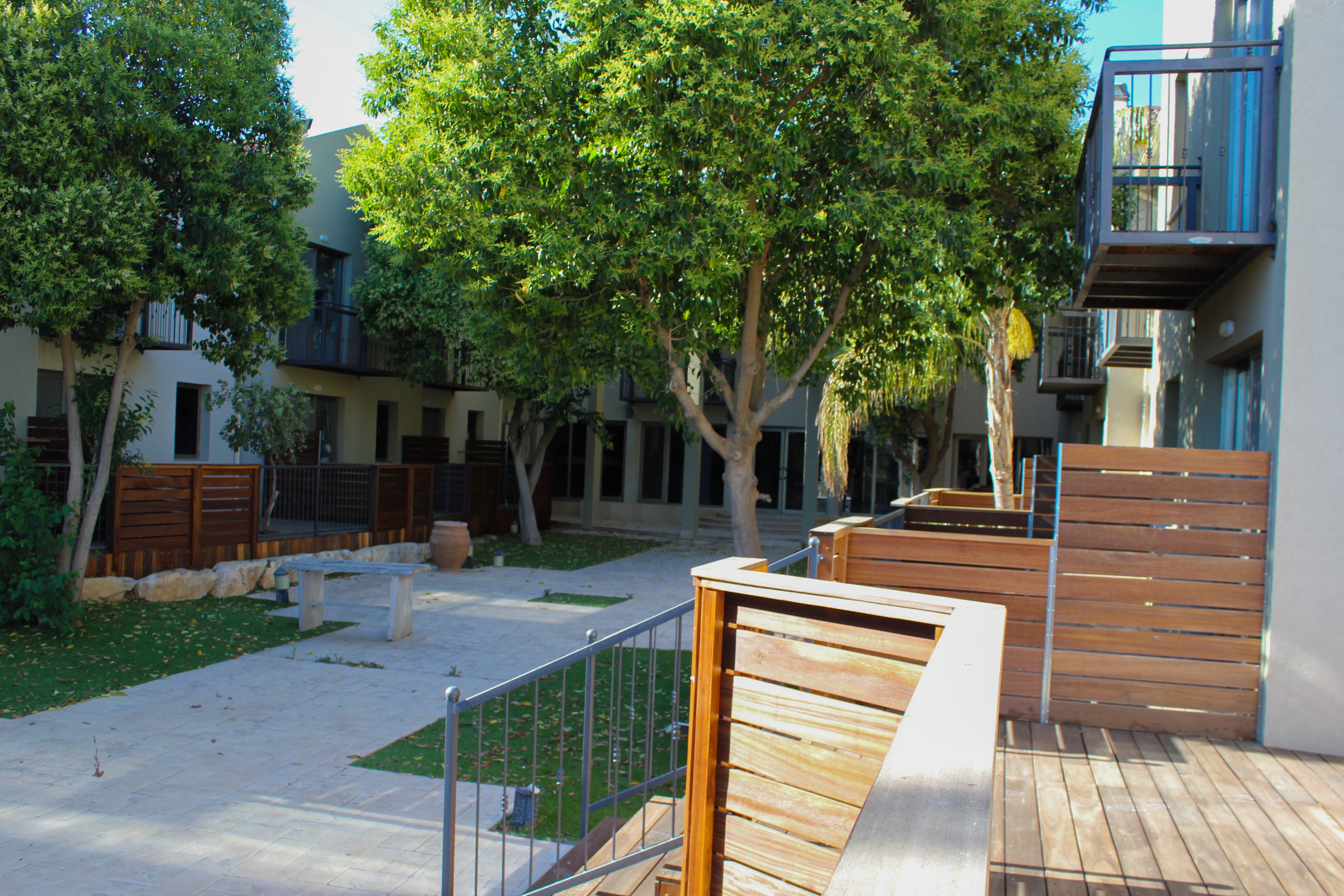 A courtyard with wooden benches, a metal fence, and trees.
