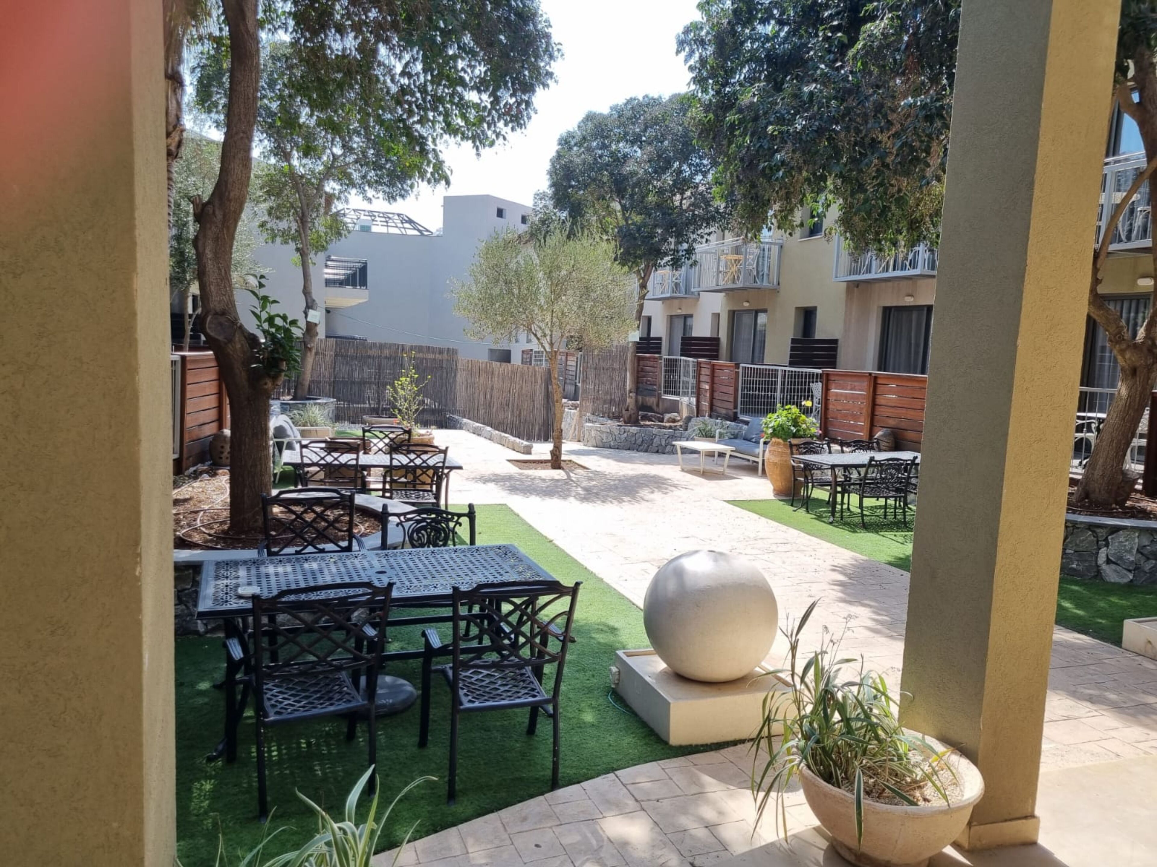 An outdoor patio with tables and chairs, surrounded by greenery and a stone wall.
