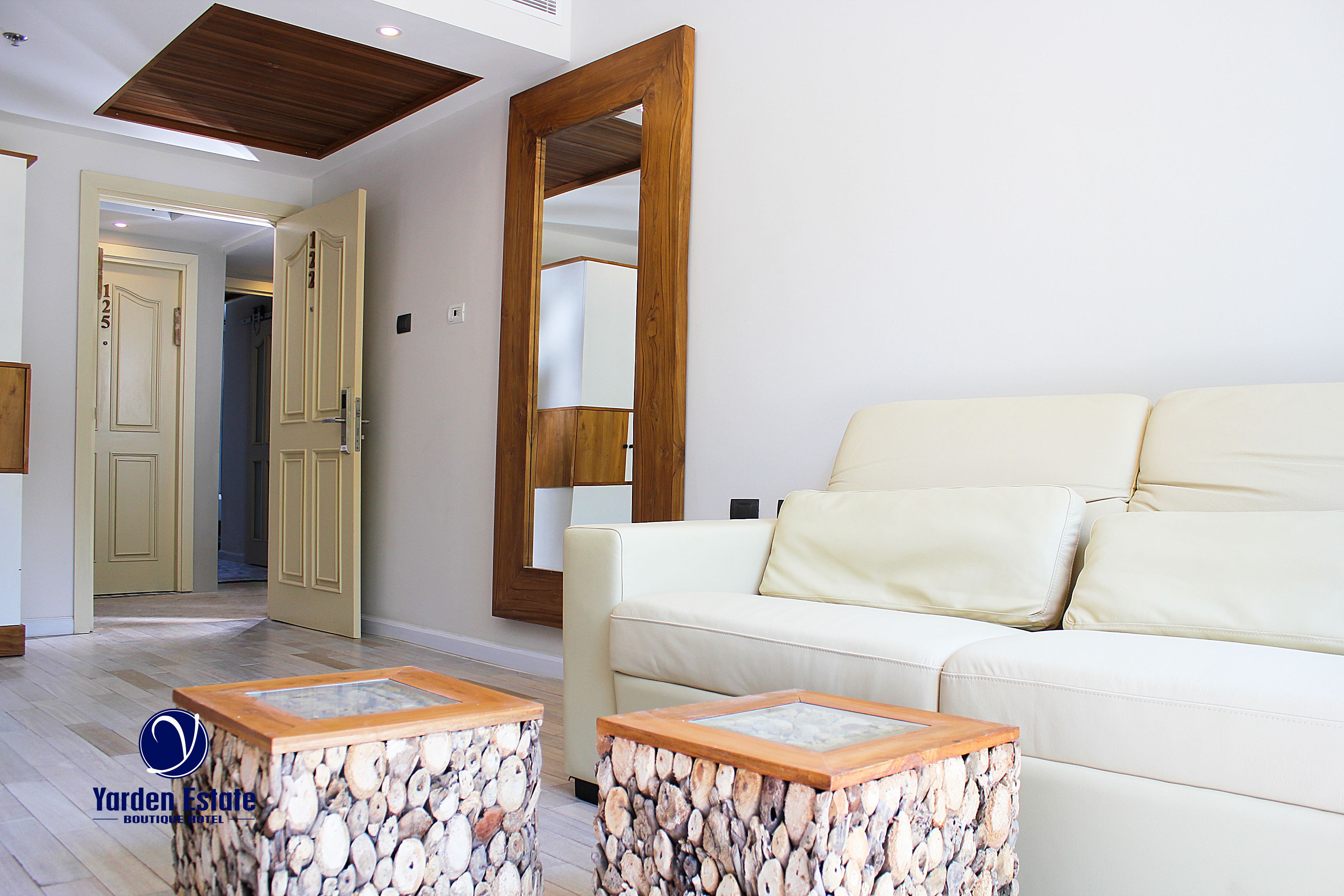 A room with a white sofa, two wooden side tables, a large mirror, and a wooden ceiling.