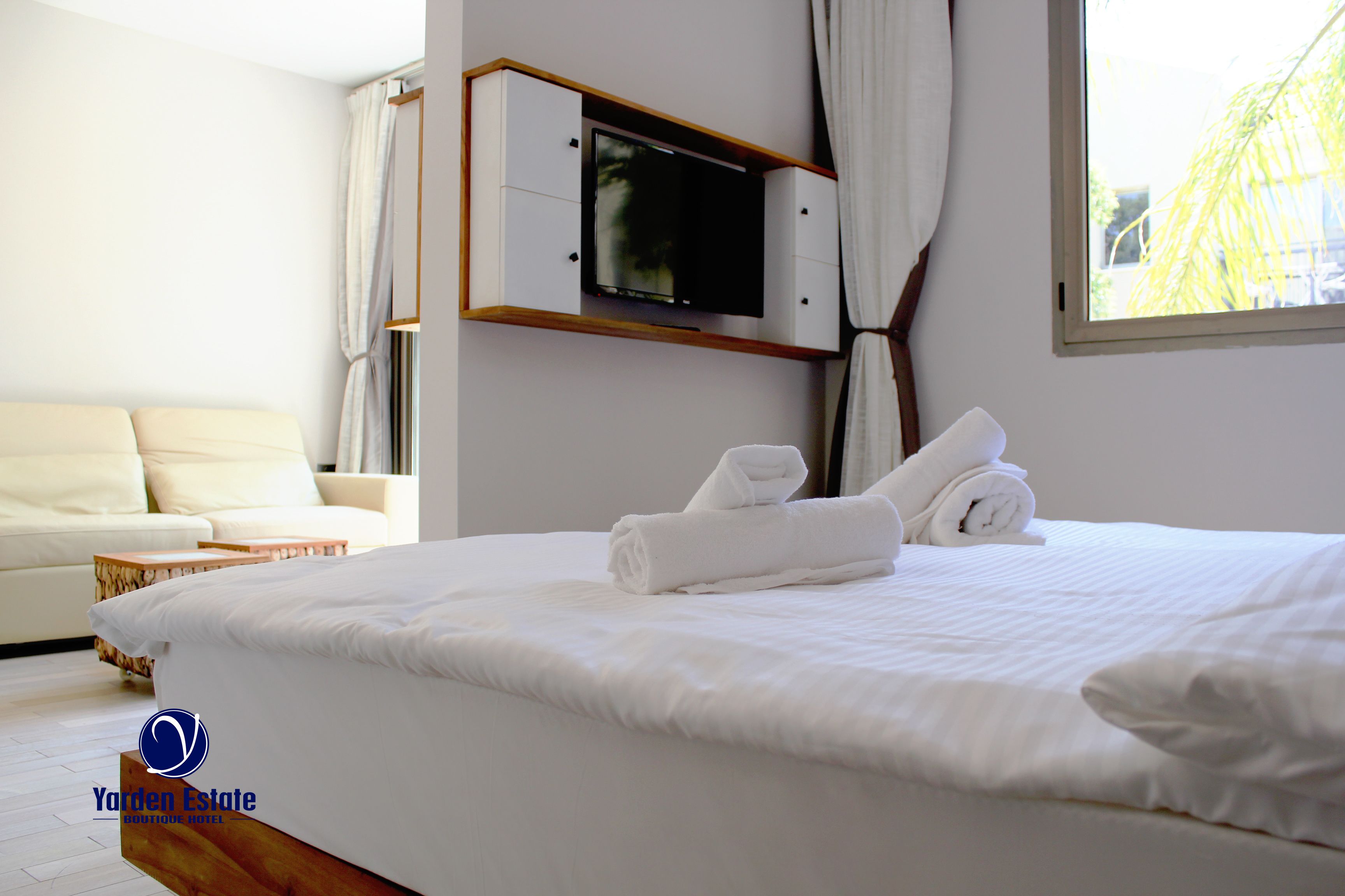 Een hotelkamer met een groot bed, een aan de muur bevestigde televisie, een bank en een raam met gordijnen.
