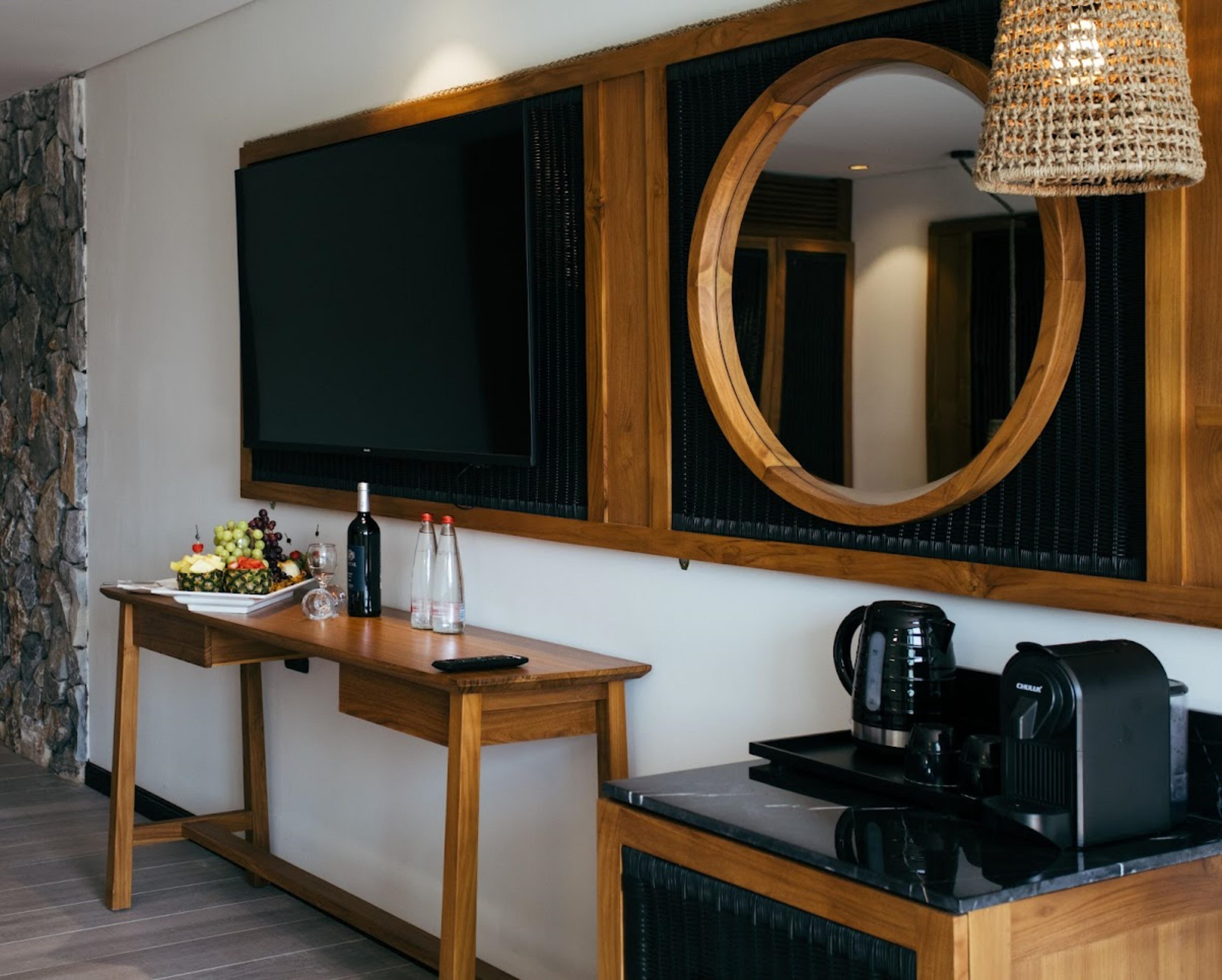 A modern room with a wooden table, a flat-screen TV, a round mirror, and a coffee maker.