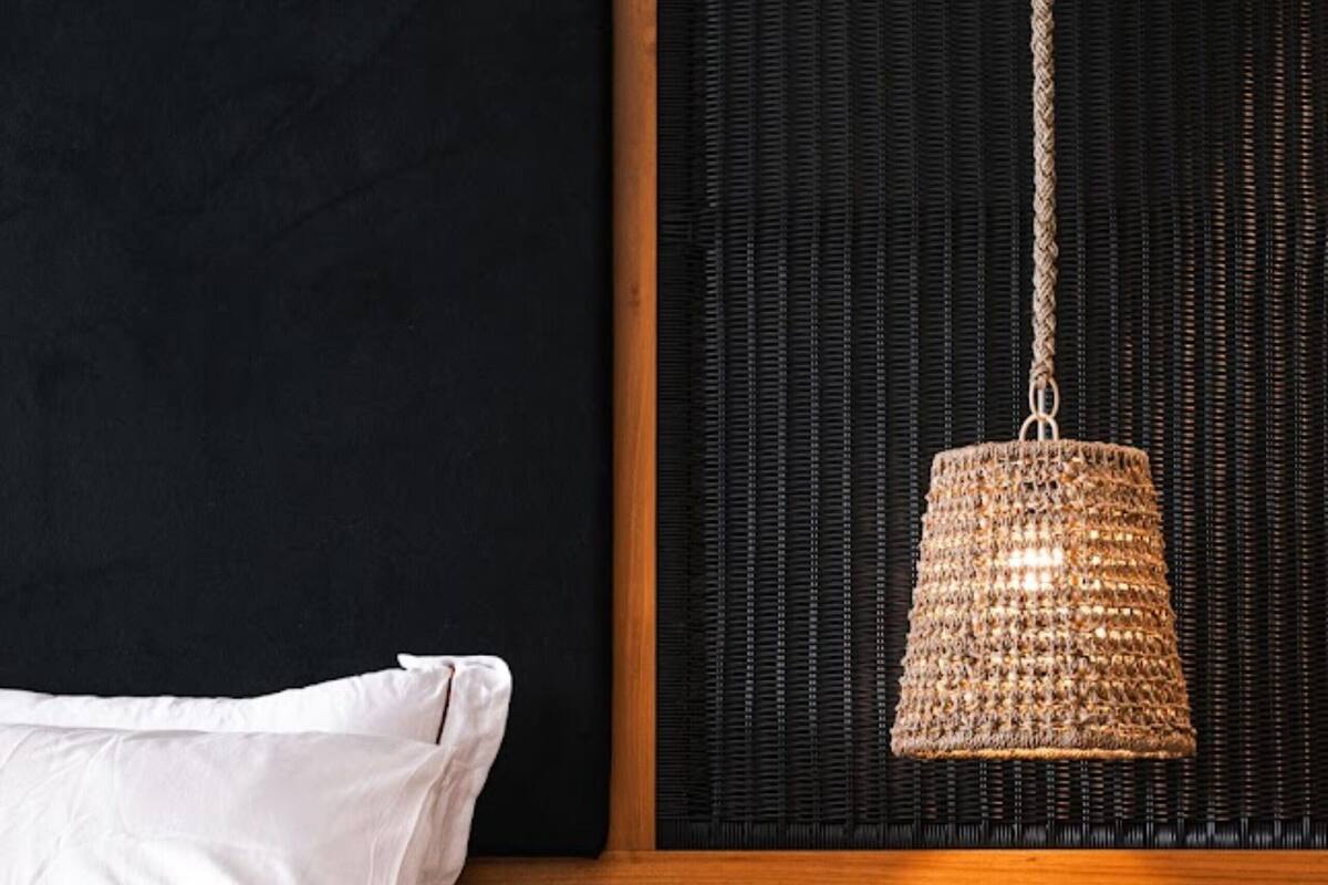 A bed with white bedding, a hanging woven light fixture, and a dark headboard with a wooden panel.