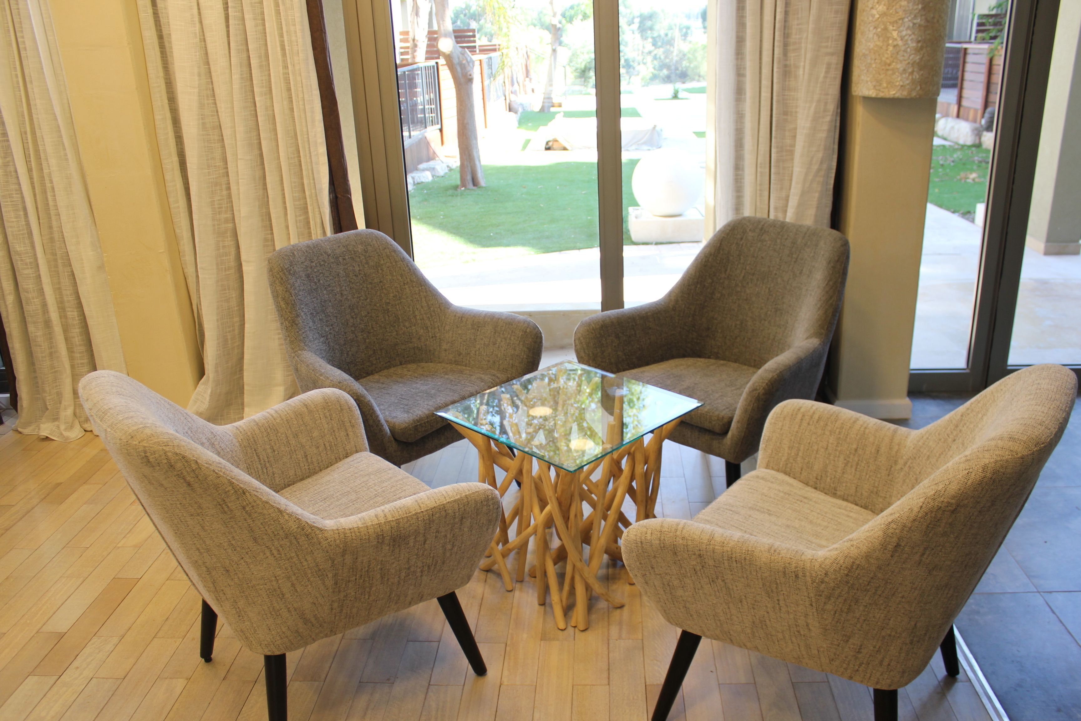Une pièce comprenant deux fauteuils beiges et une table avec un plateau en verre et des pieds en bois.