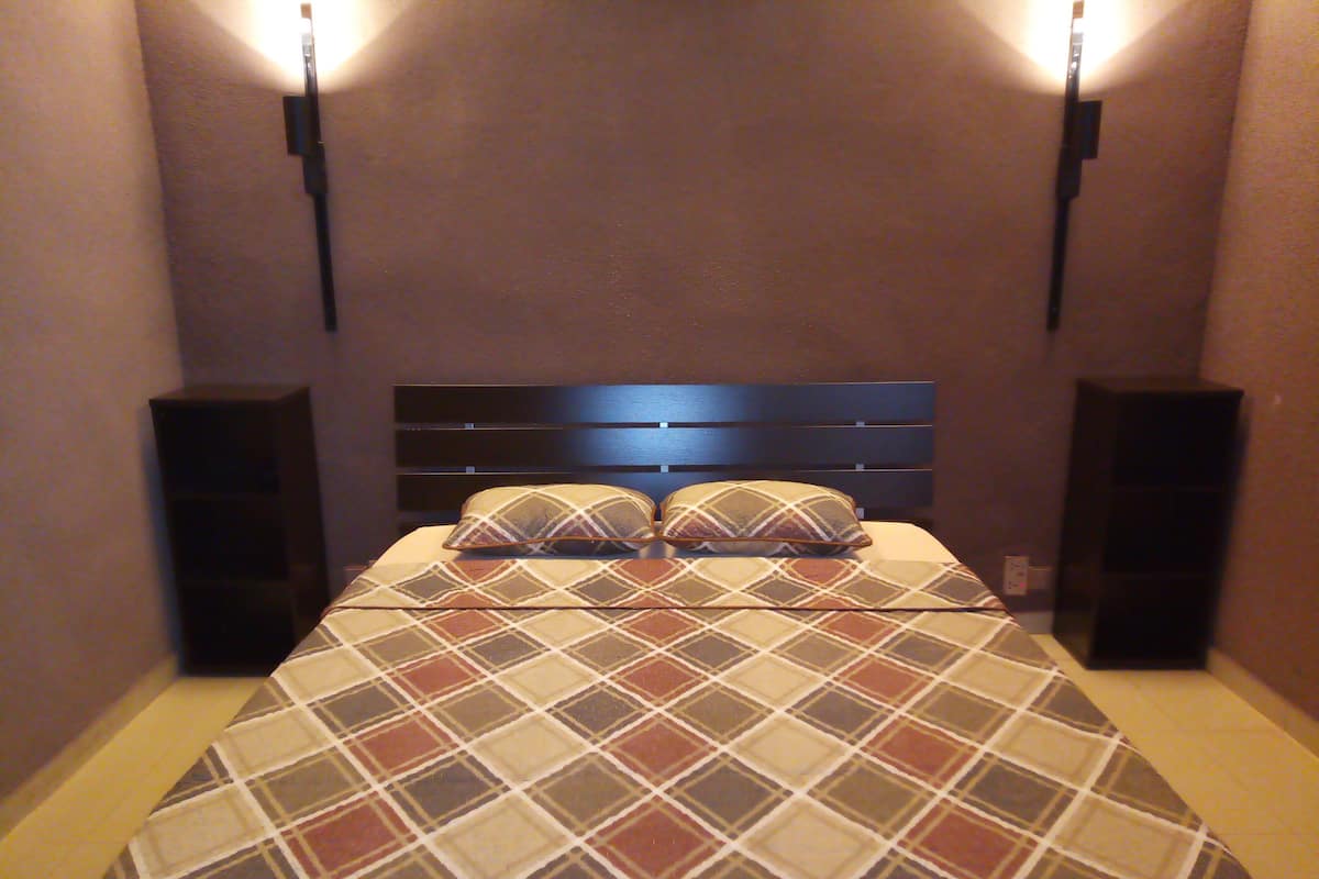 A neatly made bed with a plaid bedspread and two pillows, flanked by two speakers on either side.