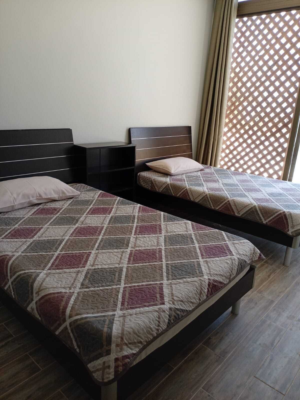 Two single beds with headboards, a wooden floor, and a window with a lattice screen.