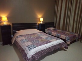 Habitación de hotel con dos camas, cada una con colcha acolchada, dos lámparas de noche y una cortina en la ventana.
