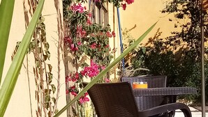Un espace extérieur aménagé avec une table et des chaises, entouré de plantes en pot et de plantes grimpantes en fleurs.