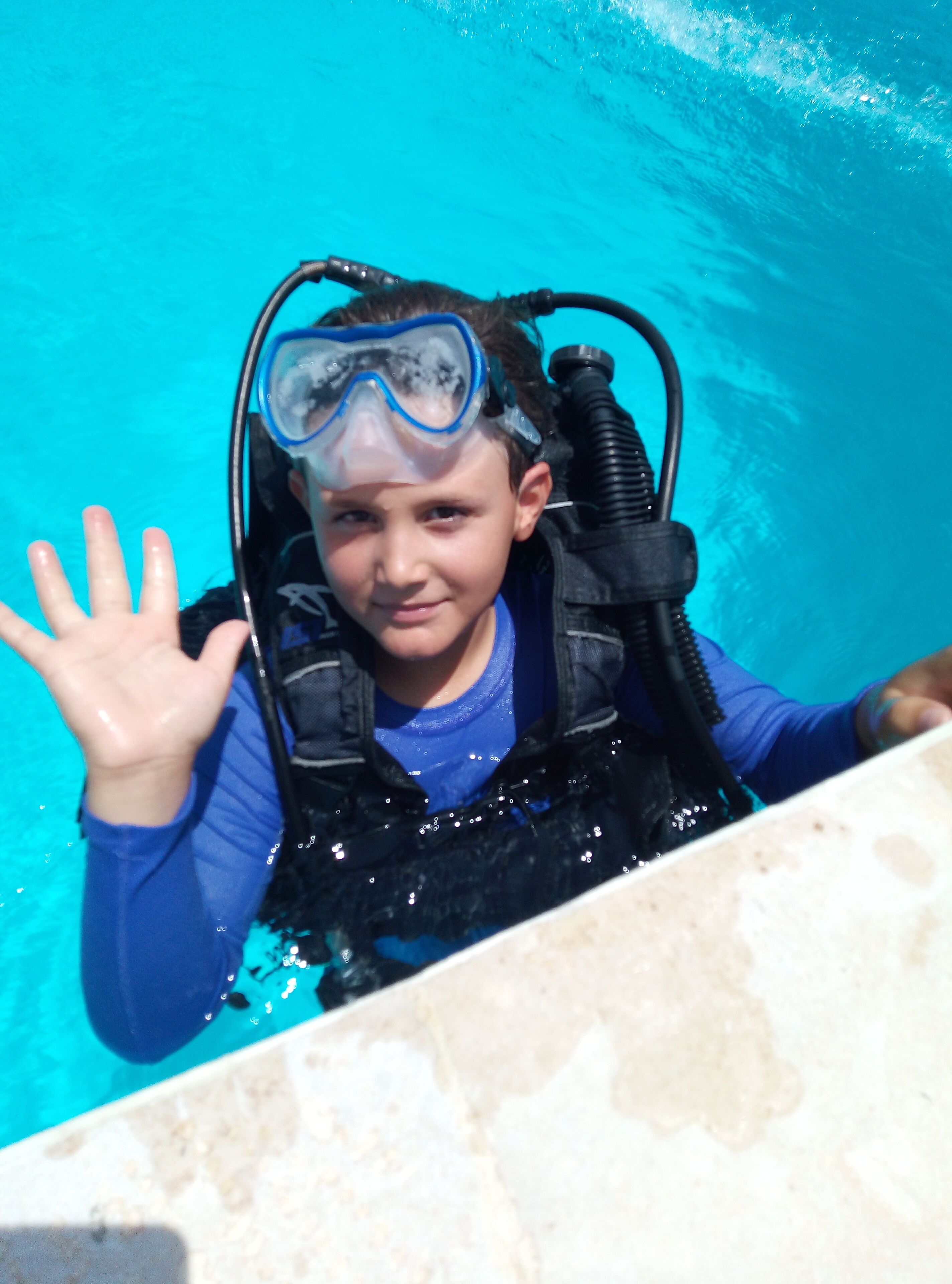 A person in a blue shirt and black life vest with a snorkel, standing in a pool.