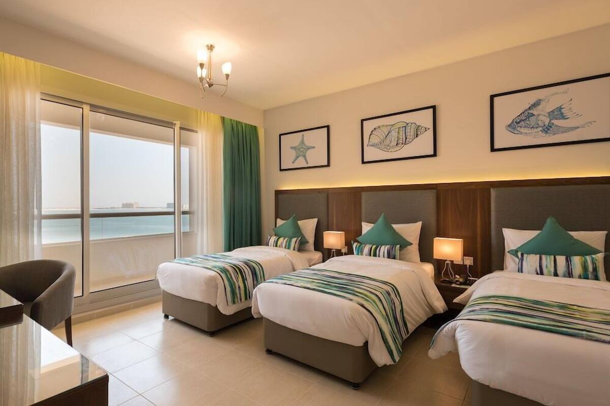 A hotel room with two beds, a desk, and a view of the sea.