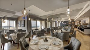 Un comedor amplio con varias mesas redondas, sillas tapizadas en gris e iluminación colgante.