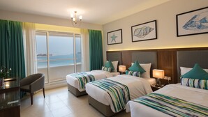 Habitación de hotel con dos camas, un escritorio, una silla y vista al mar.