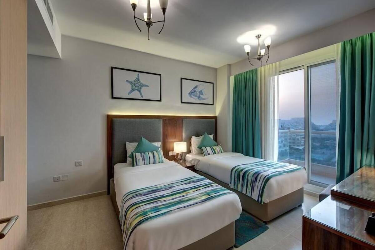Camera d'albergo con due letti, una scrivania e vista sulla città attraverso ampie finestre.