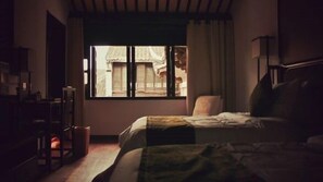 Une pièce faiblement éclairée, avec un lit, une chaise et une fenêtre donnant sur un immeuble.