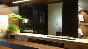 Un mostrador de recepción con una planta, un espejo y una pared con persianas verticales.