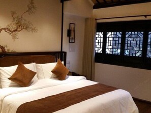 Une chambre d’hôtel avec un lit, une fenêtre ornée d’un motif en treillis et un mur décoré d’une peinture représentant une branche d’arbre.