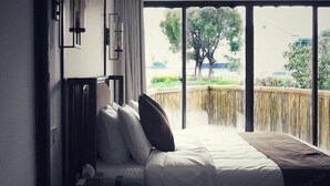 Un dormitorio con una ventana grande, una cama con almohadas, una mesita de noche y vistas a zonas verdes.