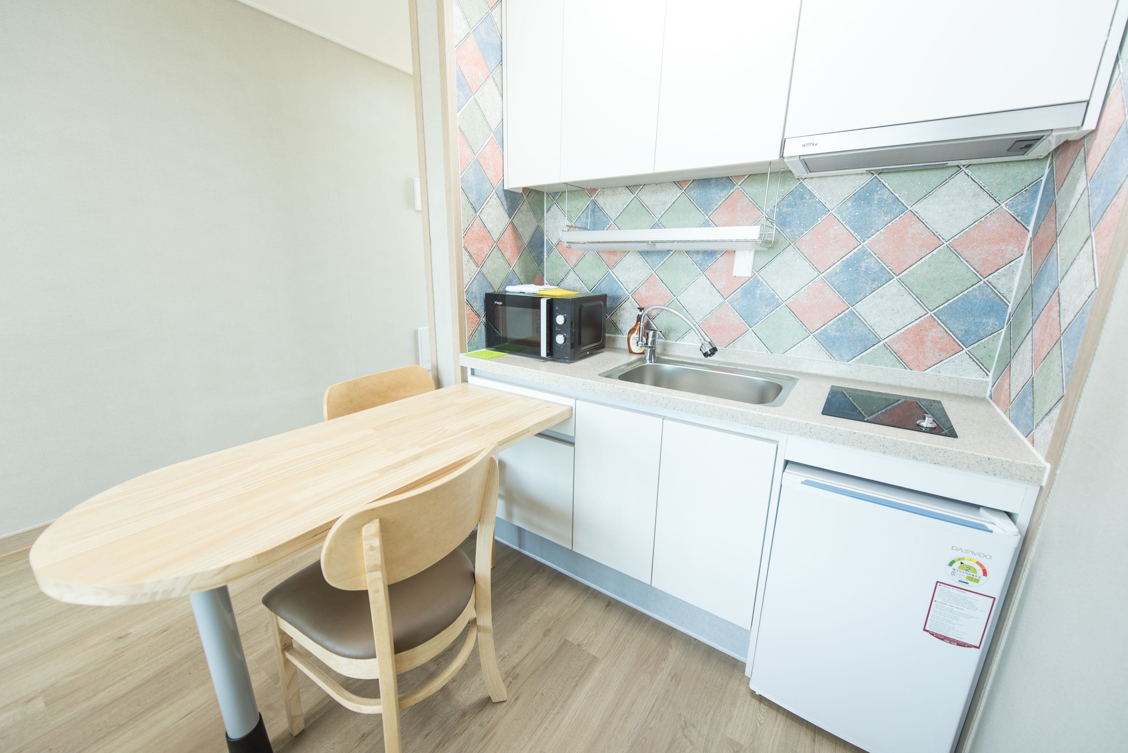 A small kitchen with a wooden table and chairs, a microwave, a sink, and a refrigerator.