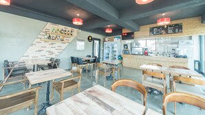 A modern restaurant interior with wooden tables and chairs, a bar area, and a staircase with a brick wall. - Pension Jung Won (Seogwipo)
