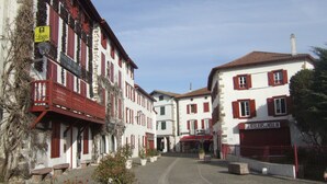 Eine Straße mit Gebäuden, die rote Fensterläden und Balkone haben, mit einem Schild für 'Logis' und einem Schild für 'Les Ateliers du Moulin'.