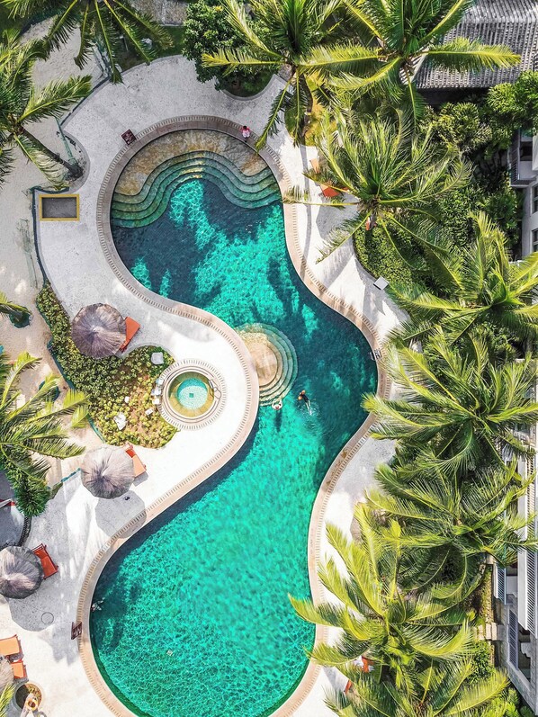 An aerial view of a resort with a large, winding pool surrounded by palm trees and a circular water feature.