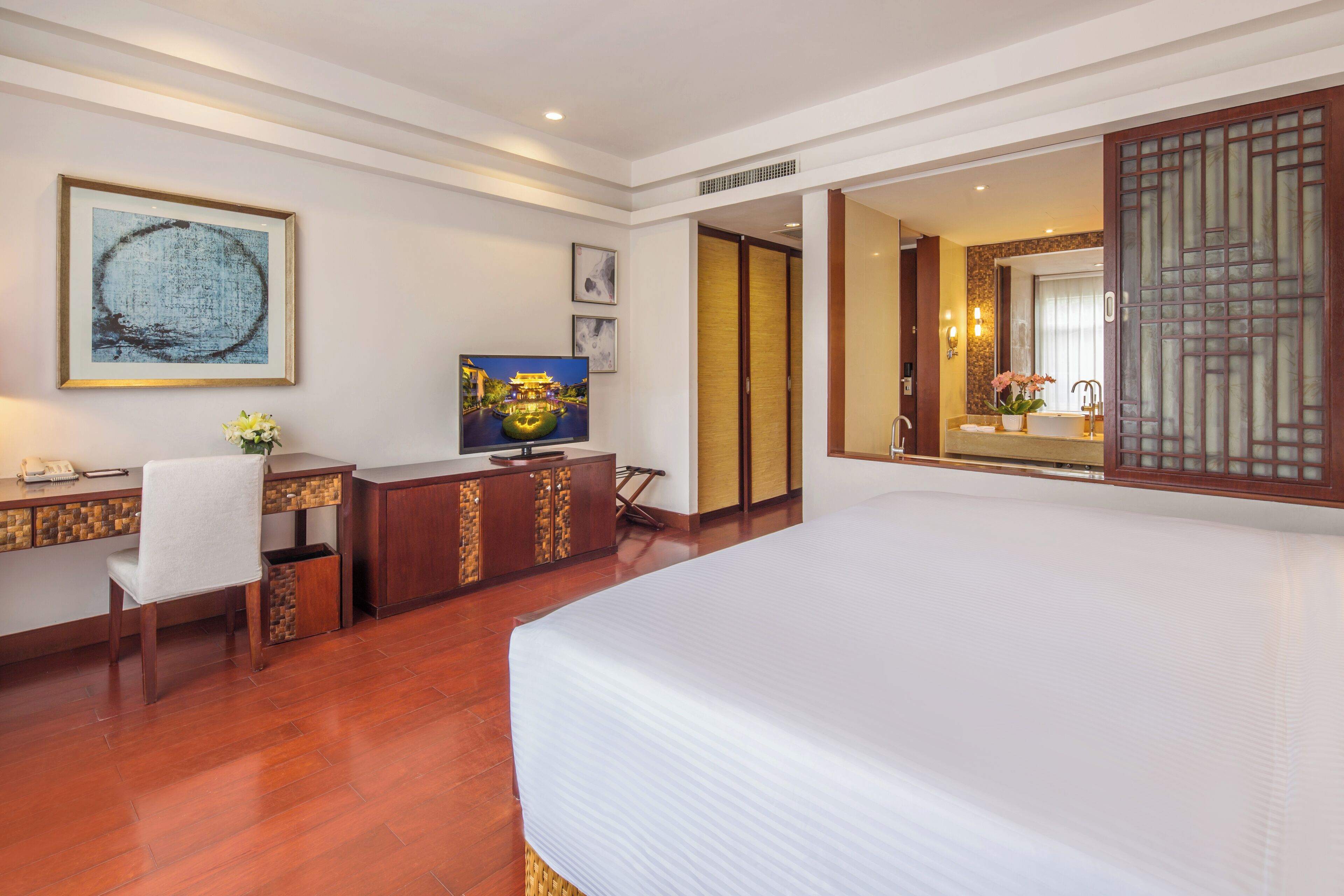 A hotel room with a large bed, a desk with a chair, a television, and a mirror.