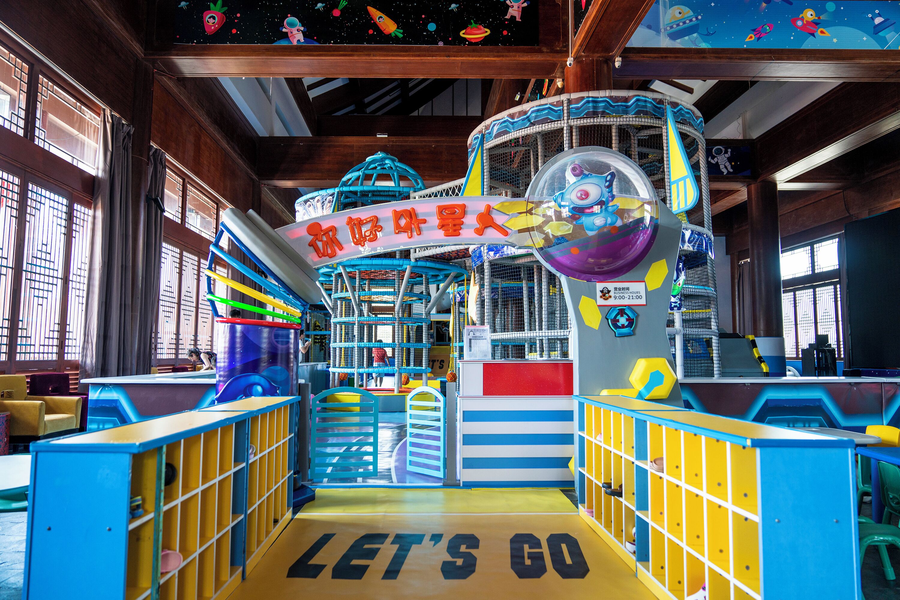 An indoor play area with a "LET'S GO" sign, colorful play structures, and a space-themed ceiling.
