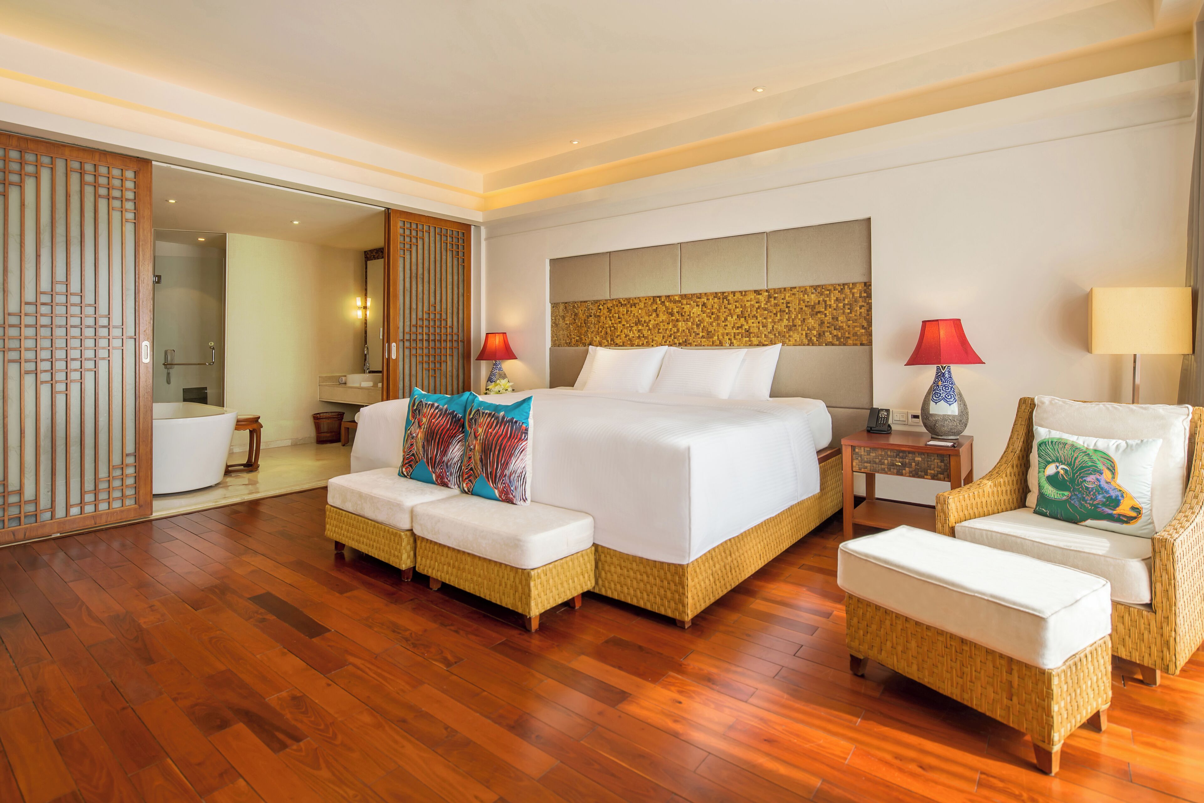 Une chambre d’hôtel avec un grand lit, deux canapés, un fauteuil et un plancher en bois.