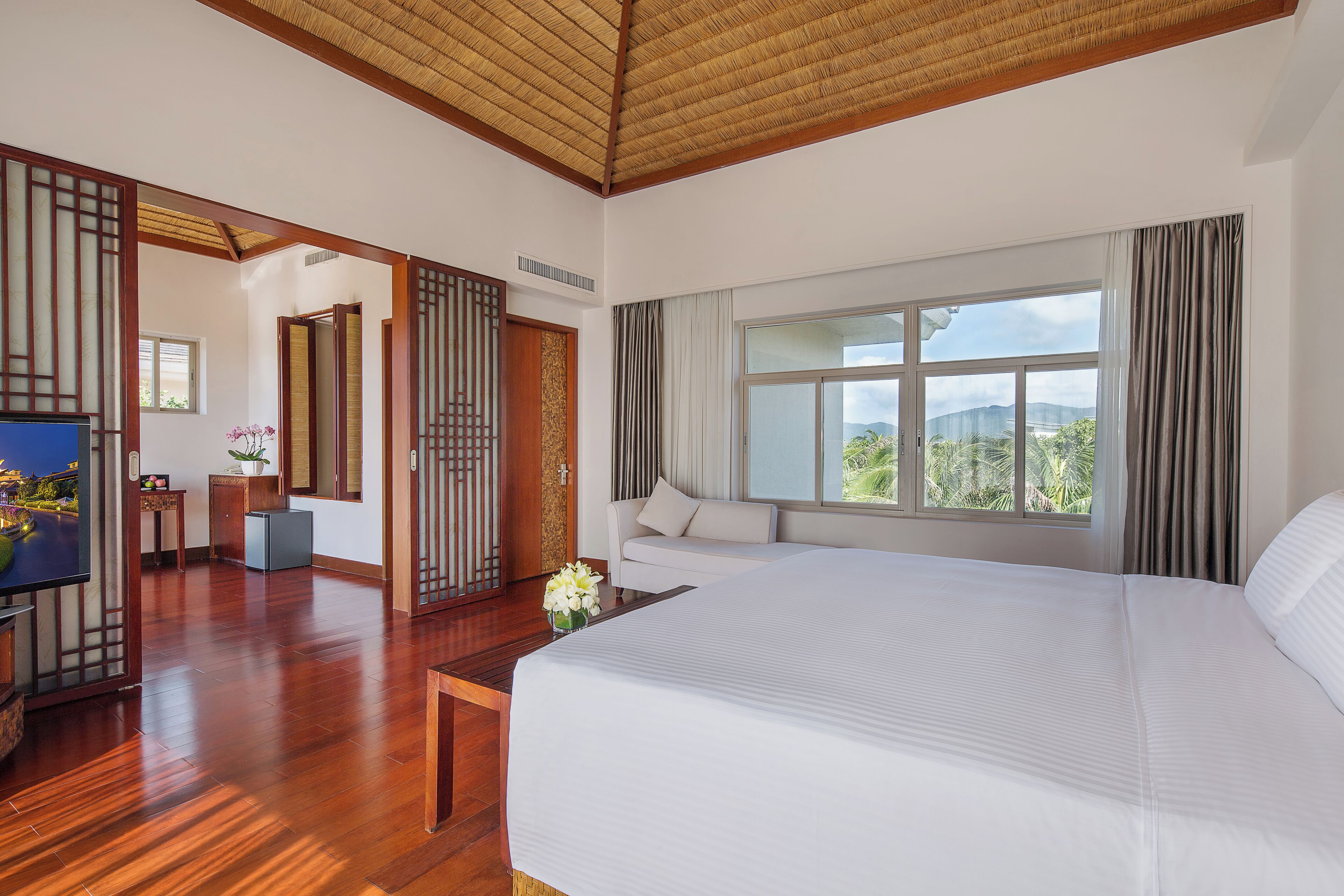 A hotel room with a large bed, a TV, a desk, and a view of the outdoors.