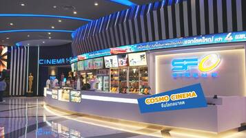 A cinema with a modern design, featuring a prominent 'Cosmo Cinema' sign and a variety of movie posters displayed outside.