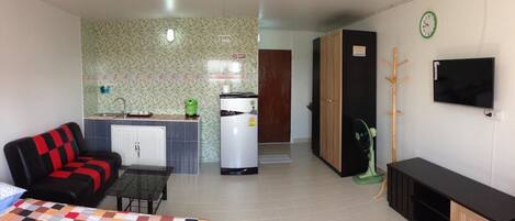 Habitación de hotel compacta con kitchenette, sofá, cama y televisor.