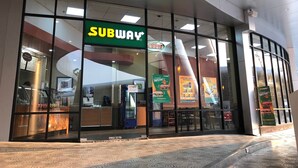Een Subway restaurant met een glazen gevel, binnenzitplaatsen en een Pepsi automaat.