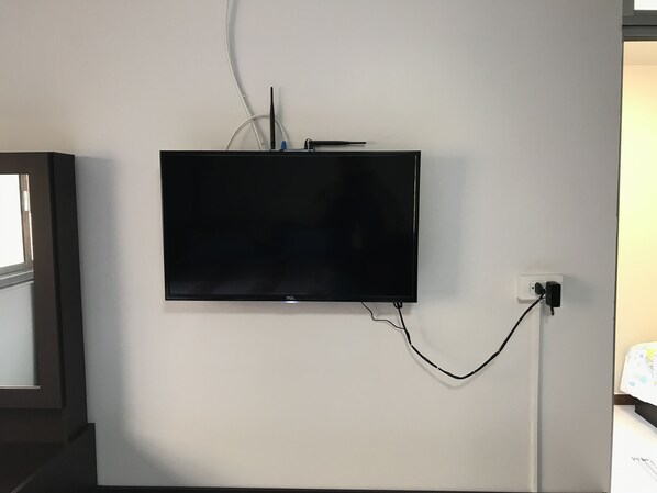 A flat-screen TV mounted on a white wall, connected to a power outlet. - Muangthongthani Rental by Khun Dan (Pak Kret)
