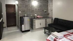 Een compacte leefruimte met een kitchenette, een koelkast, een bank en een bed.