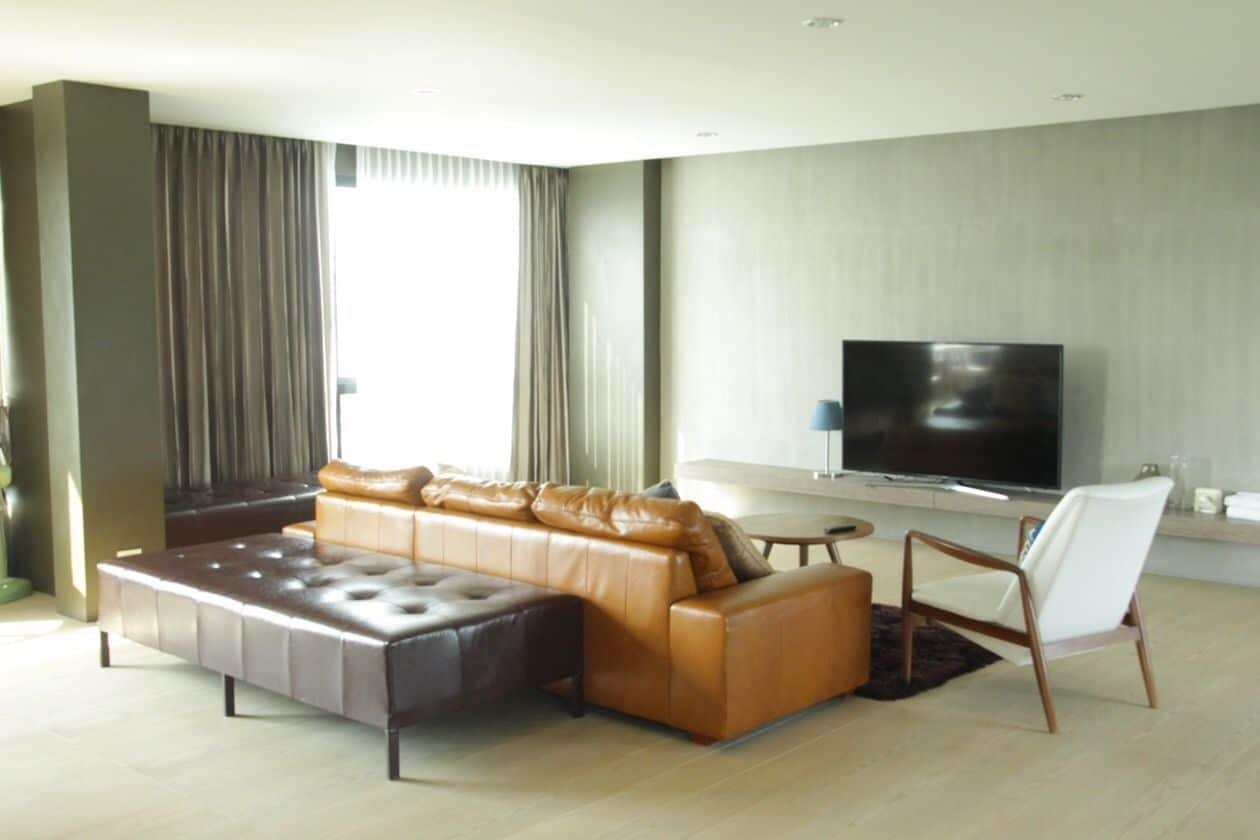 Un salon moderne avec un canapé en cuir, un fauteuil blanc et un téléviseur à écran plat.