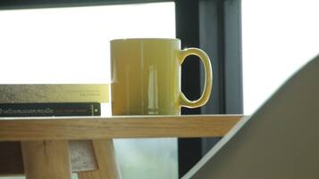 Una taza amarilla sobre una mesa de madera con libros al fondo.