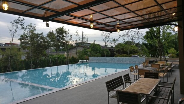 An outdoor swimming pool with a covered seating area and tables. - The Residence Thepkanjana (Krathum Baen)