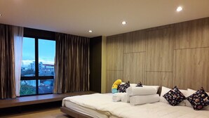 A modern hotel room with a large bed, a view of the city, and a wooden headboard. - The Residence Thepkanjana (Krathum Baen)