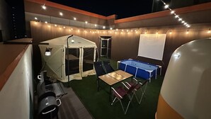 Un espacio al aire libre techado con una tienda de campaña, mesa de billar y pantalla de proyector.
