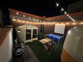 Un espacio al aire libre techado con una tienda de campaña, mesa de billar y pantalla de proyector.