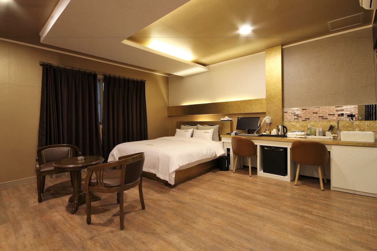 A hotel room with a bed, desk, chairs, and a kitchenette.