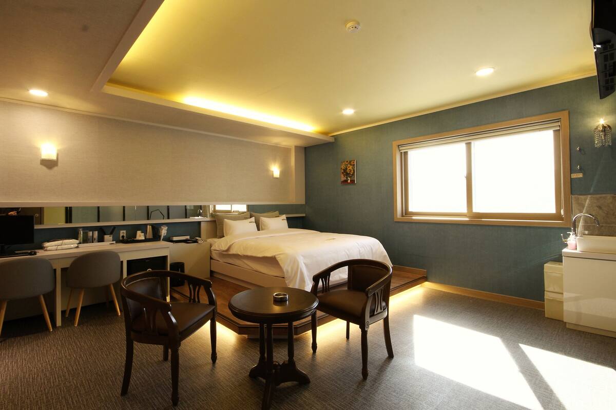 A hotel room with a bed, desk, chairs, a small table, and a window.