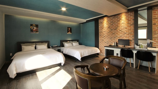 Habitación de hotel con dos camas, un escritorio con computadora y un área de comedor con sillas.